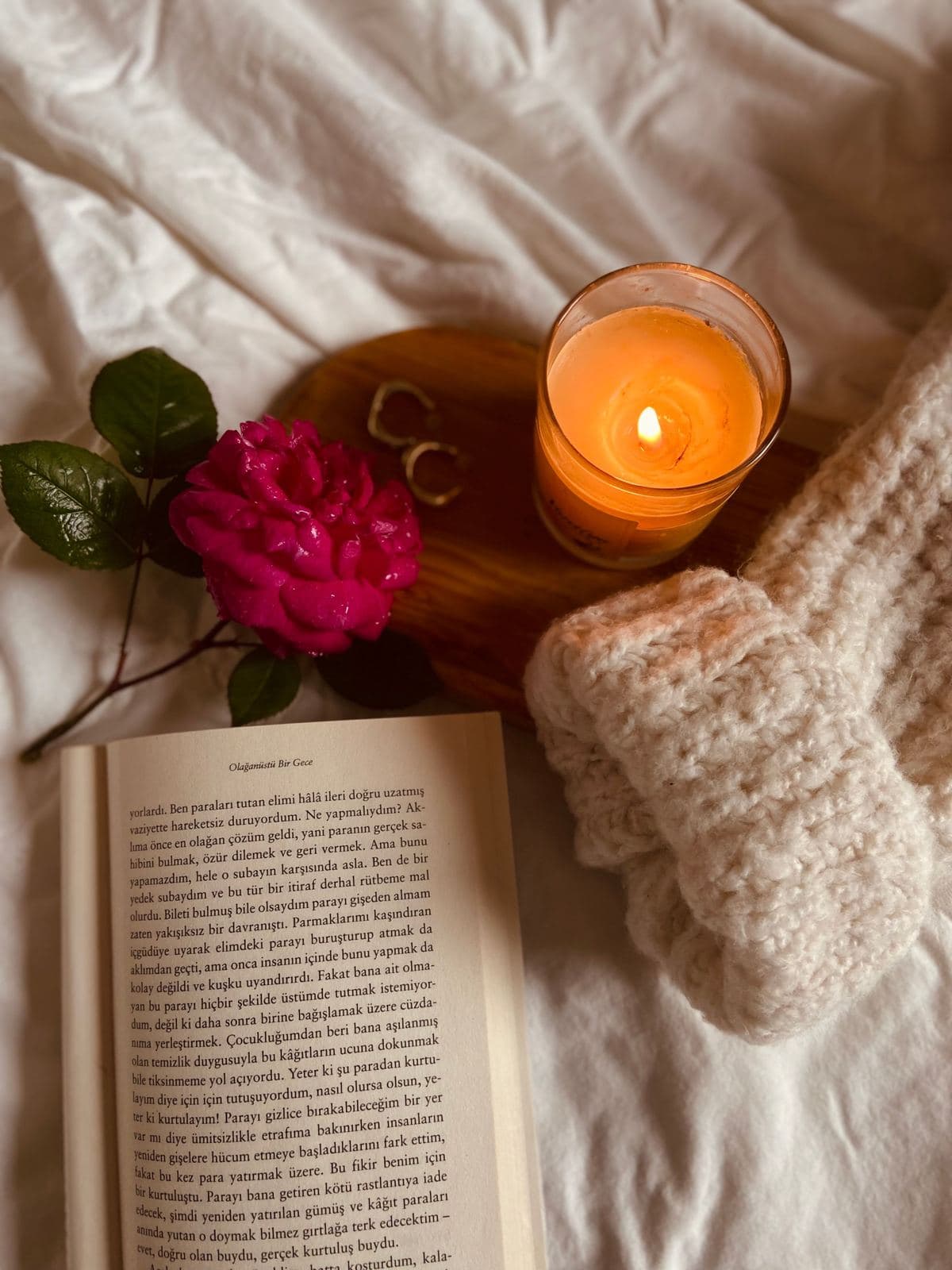 Open book beside a lit candle and a soft knit blanket